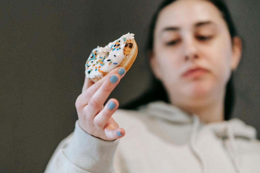 Crop emotionless female in casual wear chewing tasty doughnut glazed with vanilla icing in light room